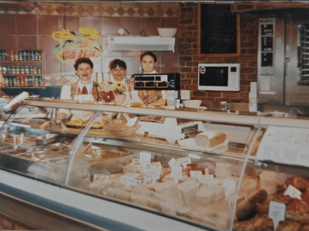 Women smiling behind a Frey's counter filled with food products, representing the longevity of women in hospitality.