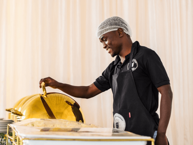 A catering professional smiling while opening a chafing dish on a buffet line.